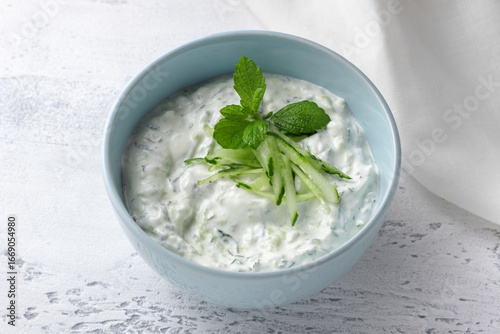 Fresh traditional Greek tzatziki sauce with yogurt, cucumber and mint light blue ceramic bowl on light background. Healthy Mediterranean appetizer, dip or dressing