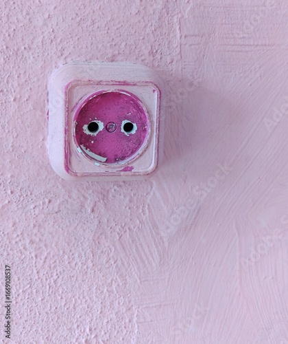 Rustic pink wall with worn electric socket in pastel interior design
