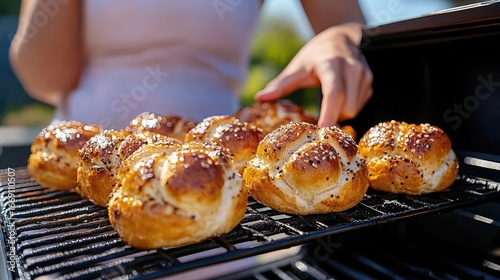 Fototapeta Naklejka Na Ścianę i Meble -  Golden Sesame Seed Buns Grilling Outdoors: Close-up of artisan bread baking on a grill, sunlit summer scene.