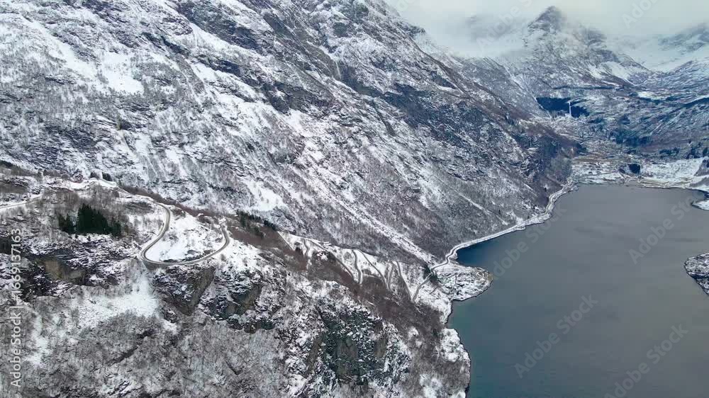 custom made wallpaper toronto digitalAerial footage capturing the winter landscape of Geirangerfjord, Norway, showcasing snow-dusted mountains, a winding road, and the deep blue waters of the fjord.