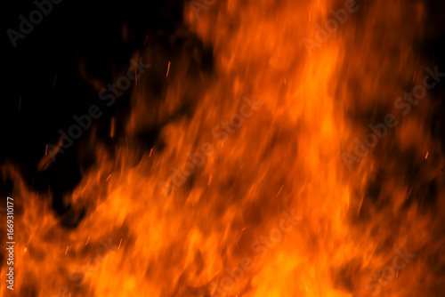 Narrow focus of a crackling bonfire at night in Brazil. Orange flames dance among stacked wood, illuminating the darkness. Sparks fly up, creating a fascinating visual spectacle.