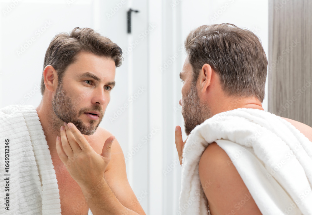 Fototapeta premium Beauty face portrait of a beautiful man applying face cream. Skincare cream for man. Mask, skin lifting and anti-aging effect. Beauty male face concept. Skincare and aging. Face cosmetic.