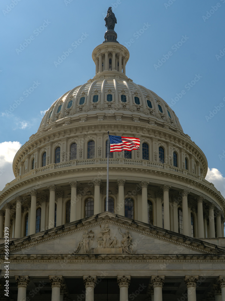 Fototapeta premium American flag waving on a flagpole against Congress and clear blue sky. US flag fluttering in the wind near Congress. USA, US waving flag, American flag.