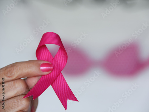 Selective focus of woman holding pink ribbon with pink bra in the background for Brest Cancer Awareness Month concept in October. 