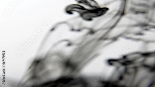Abstract black ink swirling in water, creating dynamic patterns against a soft white background