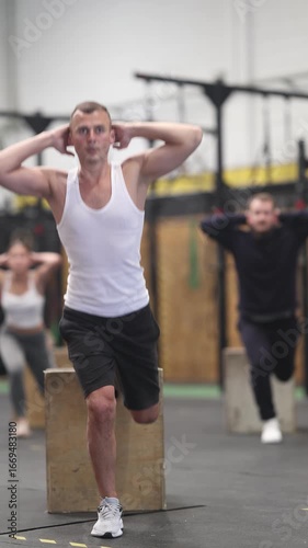 Concentrated young adult athlete performing Bulgarian split squats using wooden plyo box during cross training in gym, focusing on working out quadriceps, hamstrings, and glutes. High quality 4k