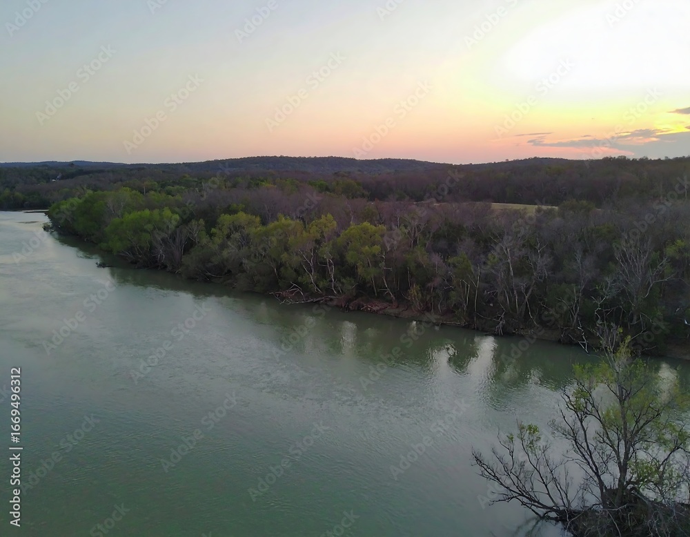 Fototapeta premium Serene sunset over a tranquil river, winding through a landscape of trees and open fields