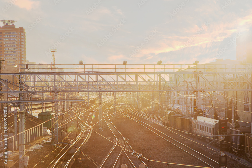 Fototapeta premium Urban railway scene at sunset with multiple tracks and buildings in the background. Soft light creates a warm atmosphere.