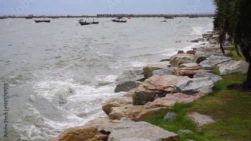 Sea waves crashing against rock with group of small boat mooring and jetty background