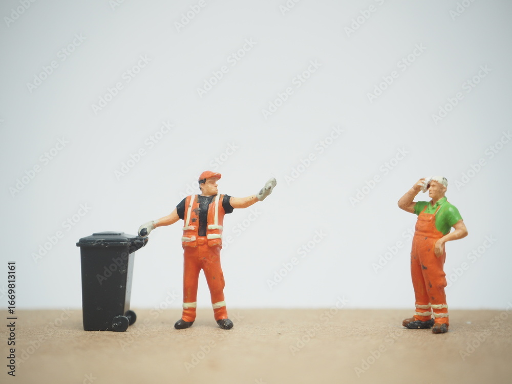 Naklejka premium Mini toy of action figure with blurred background. Miniature diorama photography concept design. Minifigure of cleaning crew character wearing orange suit with truck and garbage bin.