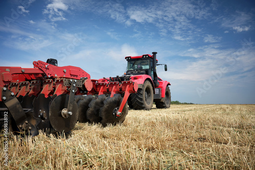 Rear view of a large tractor with a disk harrow plow standing in a field. Start tillage after harvest.