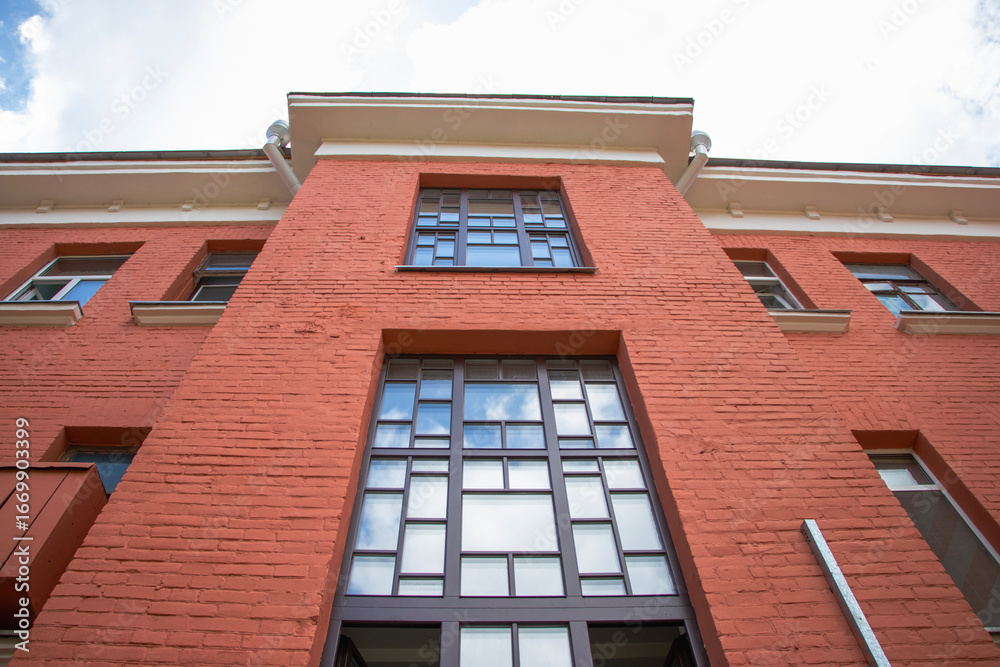 Obraz premium Bright red brick building stands tall against a blue sky with scattered clouds in an urban setting