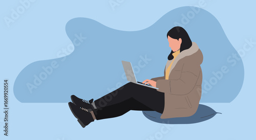 Focused person in a warm jacket working on a laptop while sitting comfortably on a cushion. Represents remote work, online learning, or a relaxed digital lifestyle.