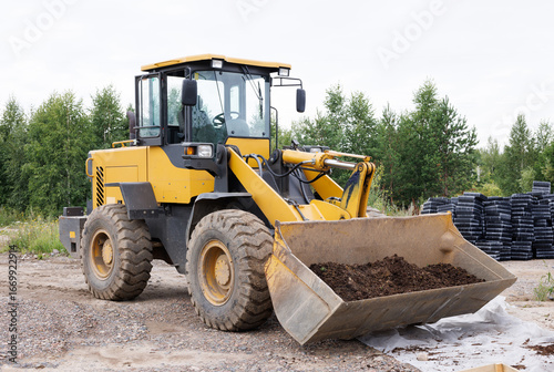 Yellow loader with bucket against the background of nature.
