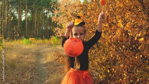 Halloween kids going to collect candy. Trick-or-treating. Child in carnival costume witch outdoors. Celebrate halloween. Girl in autumn forest smiling and holding of sweets candy