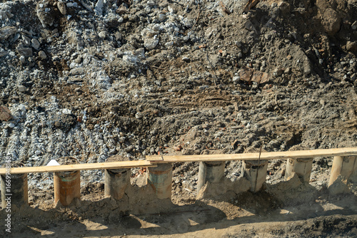 Quadro em tela Construction site ground view with excavated earth, demolition debris, and row of concrete pipe foundations topped with wooden planks