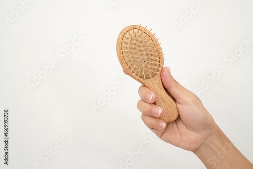 Woman hand holding wooden hairbrush on white background, copy space