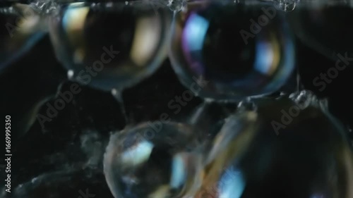 Soap bubbles shimmer and burst in slow motion, catching rainbow reflections against a dark background.
