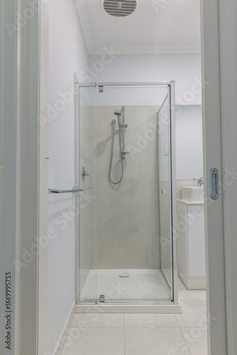 Modern tiled shower with glass enclosure in residential bathroom, minimalist design featuring chrome fixtures and neutral wall tones