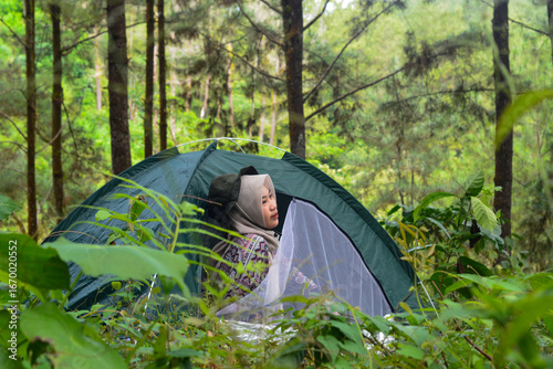 Portrait of young Asian woman camping with small tent for solo camping in forest, with nature and cow background