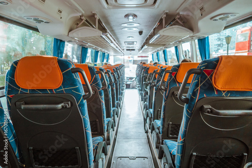 rows empty seats with orange headrests fill interior well-maintained bus. blue curtains line windows, enhancing atmosphere quiet travel experience. close up.