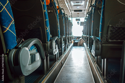 rows seats are lined up in modern bus, featuring vibrant blue fabric and ample legroom. bright exterior light illuminates aisle, enhancing travel atmosphere. close up.
