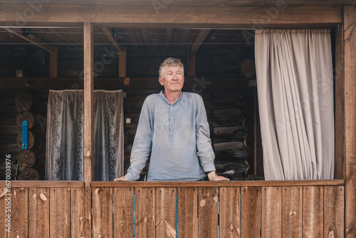 handsome man middle aged stands relaxed on wooden balcony, taking in serene surroundings rustic cabin. sunlight filters in, creating calm atmosphere in nature. close up.