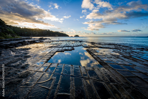 Sunrise over tessellated rock formations on a quiet coastal shelf by the sea.