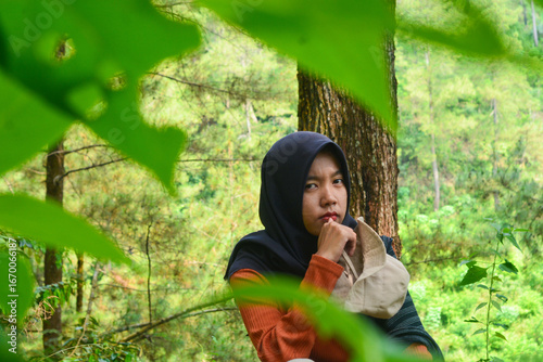 Young Asian Muslim woman hiking and camping in autumn forest, smiling at camera wearing Javanese ethnic clothes