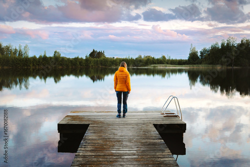 Canvas Print Woman traveling solo in Finland standing alone on pier enjoying sunset lake and