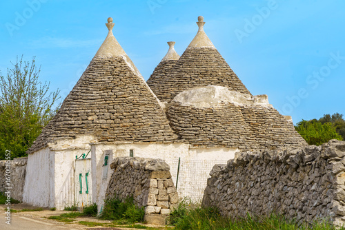 Traditional trulli houses in Valle d’Itria, Apulia, Italy. Stone cone-roof dwellings, whitewashed walls and rustic dry stone fences under blue sky.