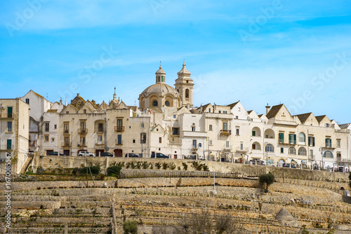 Closer view of Locorotondo historic center in Apulia. Terraced vineyards and whitewashed houses frame the impressive dome and bell tower of San Giorgio Church.