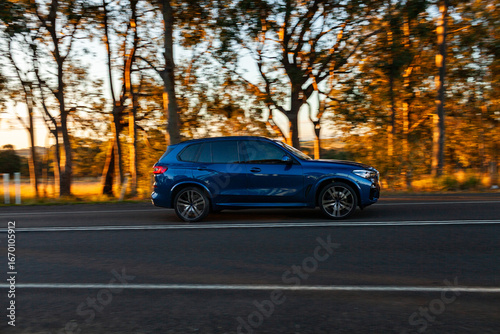 Motion blur panning image of blue suv car driving past on sealed rural country road in sunset light