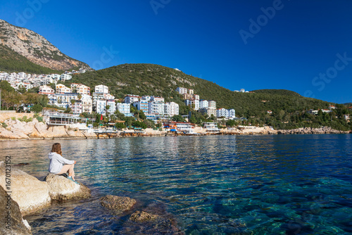 Woman looking at sea and historical town Kash placed on hills by coast of mediterranean sea in Antalya region in Turkey. Capturing summer vacation, popular place for family travel with kids.