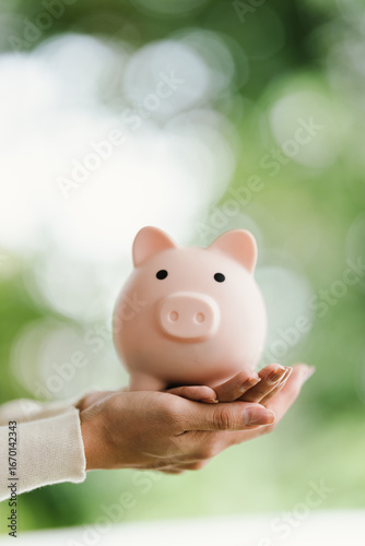 A person holds a pink piggy bank while inserting a coin, symbolizing saving, investment, financial planning, wealth protection, security, growth, and responsibility for a stable future.