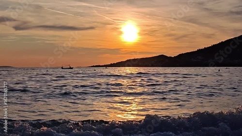 Boat at golden sunset on calm sea with mountain silhouette