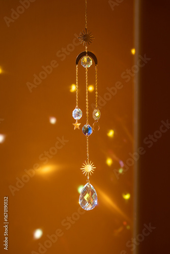 Glass suncatcher with metal golden chains, shining in sunlight and reflecting the rainbow on a yellow background
