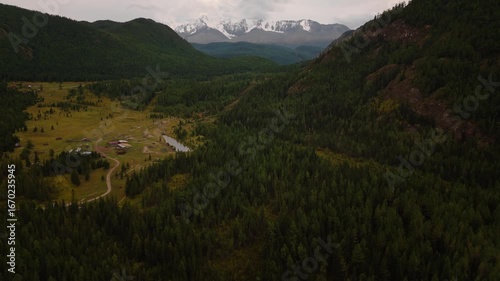Aerial drone footage of Belukha Mountain, the highest peak in Altai, Russia. Snow-capped ridge with cloudy sky above valleys and hills. Ideal for travel, adventure, and nature projects.