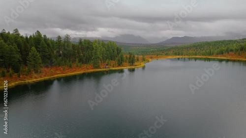 Drone shot of Kidelu Lake in Altai, Siberia. Clear water, pine forest, and vibrant autumn landscape create a stunning wilderness scene ideal for outdoor and nature projects.