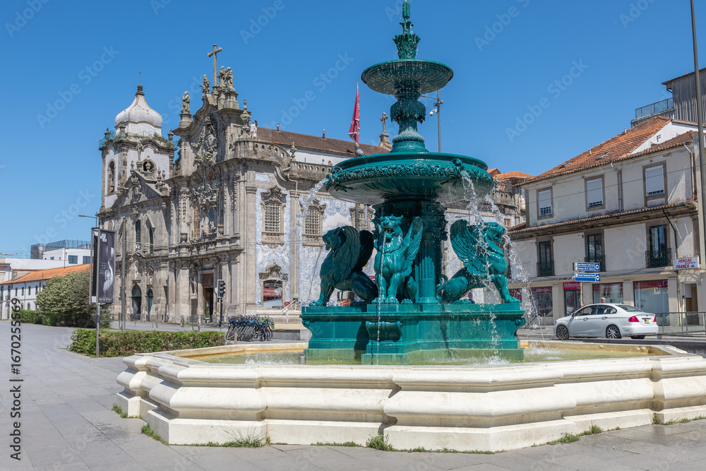 Fototapeta premium View of the Lions Fountain in Porto's square, with water flowing and the twin churches in the background on a calm, sunny day.