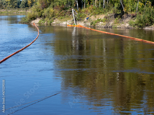Photos Orange oil containment booms on a river, used to prevent the spread of oil pollution or to collect floating debris
