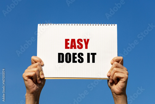 Easy does it text on paper holding by a woman's hand with blue sky background