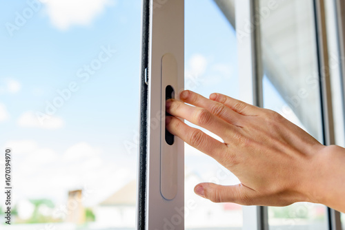 Hand opening white plastic sliding window on balcony.