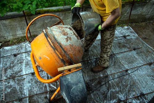 Tableau sur toile A man pours sand into a small concrete mixer