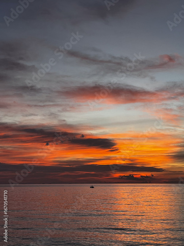 Beautiful tropical sunset over the sea with colorful sky, clouds and sun reflection on the water. Scenic evening view at Koh Phangan island, Thailand. Perfect vacation and travel background.