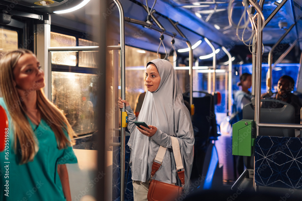 Fototapeta premium Muslim woman holding smartphone on a bus with nurse standing near