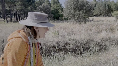 Professional biologist conducting detailed ecological research. Walking through mediterranean scrubland during sunny summer day