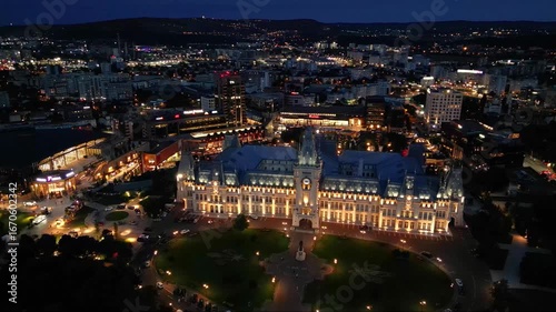 Aerial drone footage of the Iasi cultural palace in the city of Iasi in Romania at night. Beautifully illuminated palace of culture in moldavia. High angle flyover shot of evening urban cityscape.
