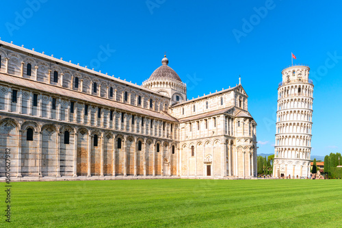 Leaning Tower of Pisa and Pisa Cathedral in Italy, showcasing Romanesque architecture under a clear blue sky with green grass in the foreground.