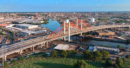 Numerous cars move by the Kosciuszko Bridge over Newtown Creek in New York City, connecting Greenpoint in Brooklyn to Maspeth in Queens. A large cemetery is situated near the river.